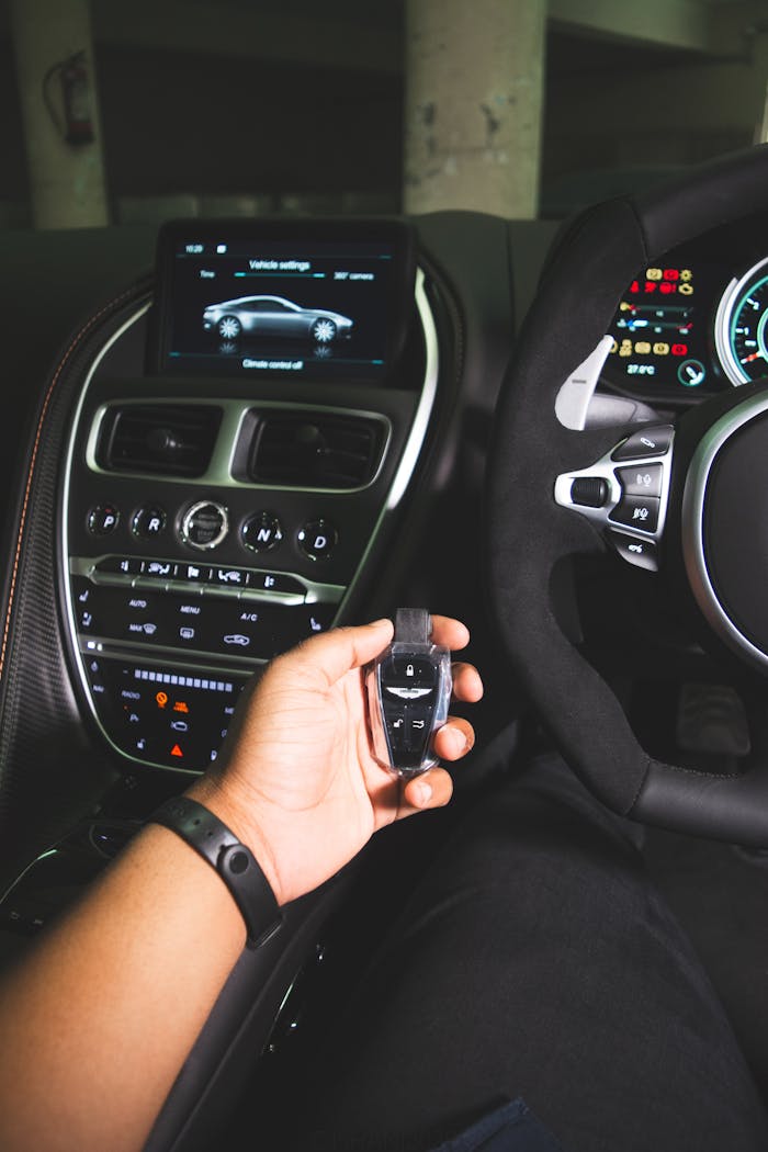 gallery-05 Close-up of hand holding a key fob in a luxury car interior with focus on dashboard and steering wheel.